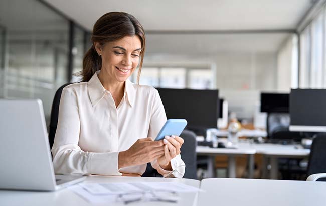 Professional woman engaging with LinkedIn Ads campaign on smartphone in office setting