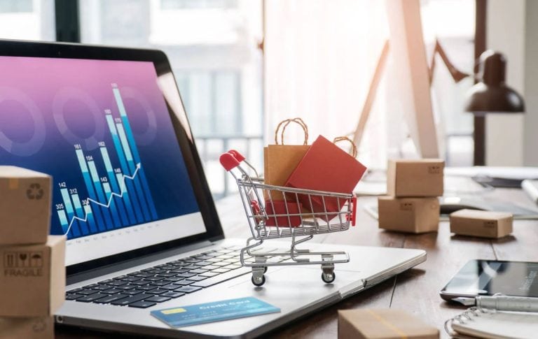 Ecommerce growth dashboard on screen with cart and packaging on desk — represents performance outcomes of keyword strategy